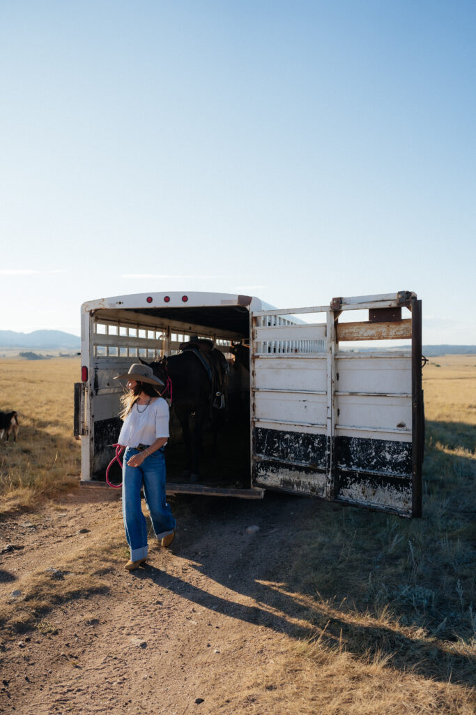 woman leading horse off a trailer while looking off in the distance