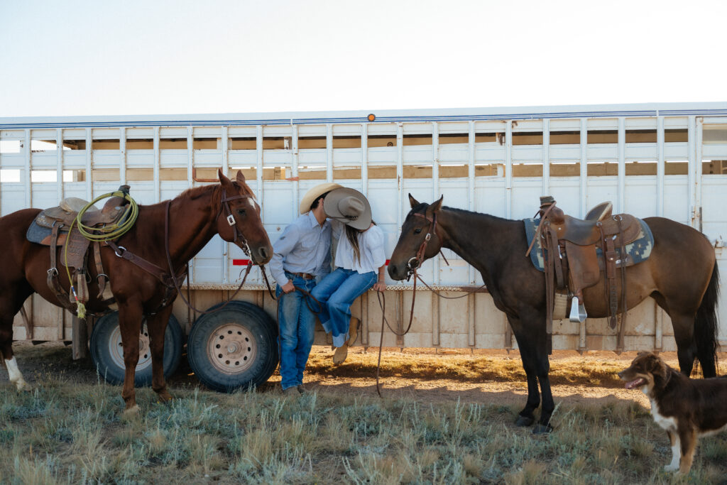 man and woman kidding while sitting on the side of a trailer with horses